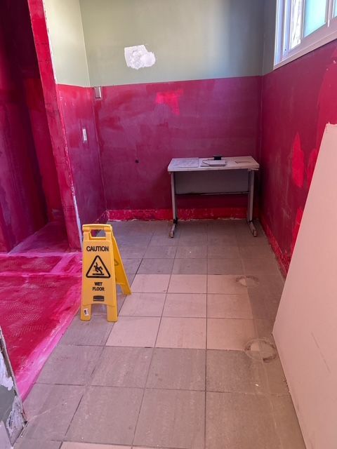 Bathroom under construction with red walls, yellow caution sign, and unfinished floor.