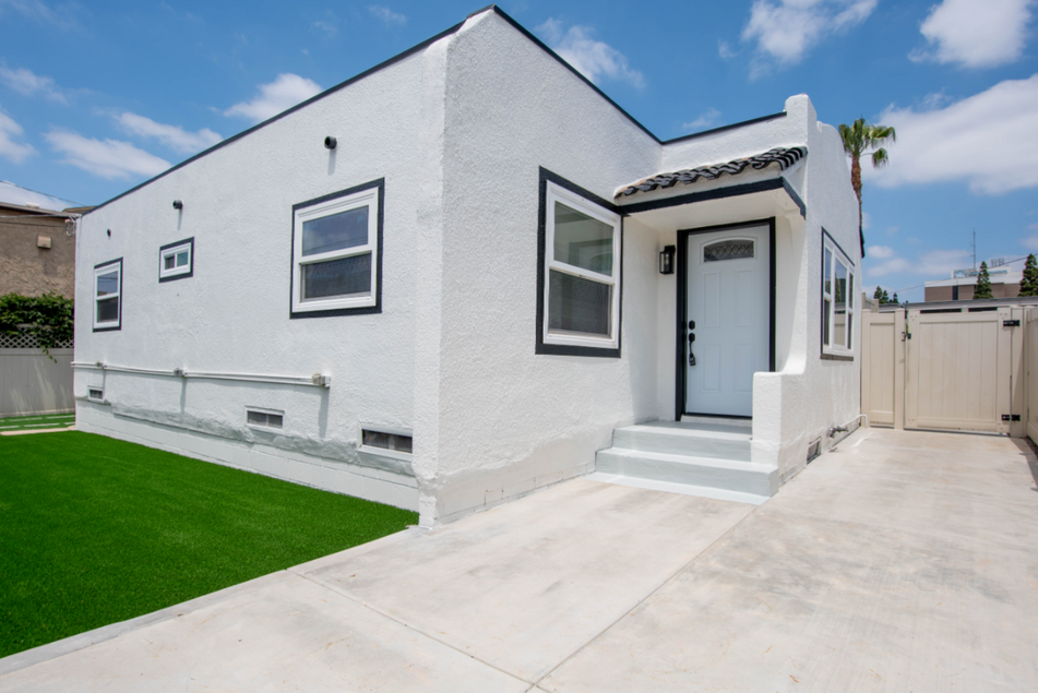 White single-story house with a front door, driveway, and small green lawn under a blue sky