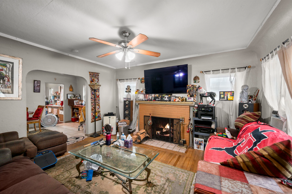 Living room with fireplace, ceiling fan, glass coffee table, TV, and colorful sofa with blanket