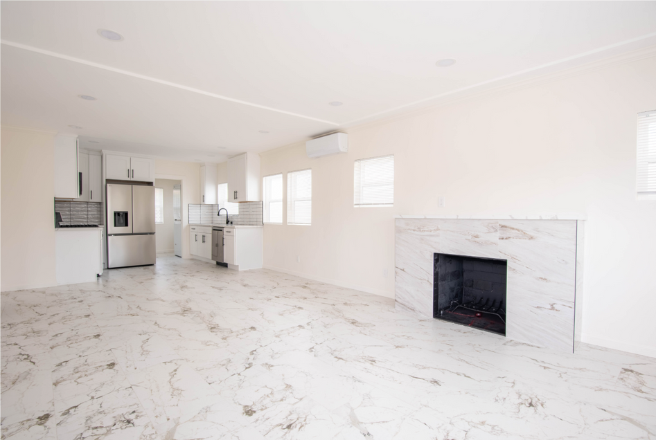 Bright empty living room with marble floors, white walls, and a black fireplace near a kitchen area