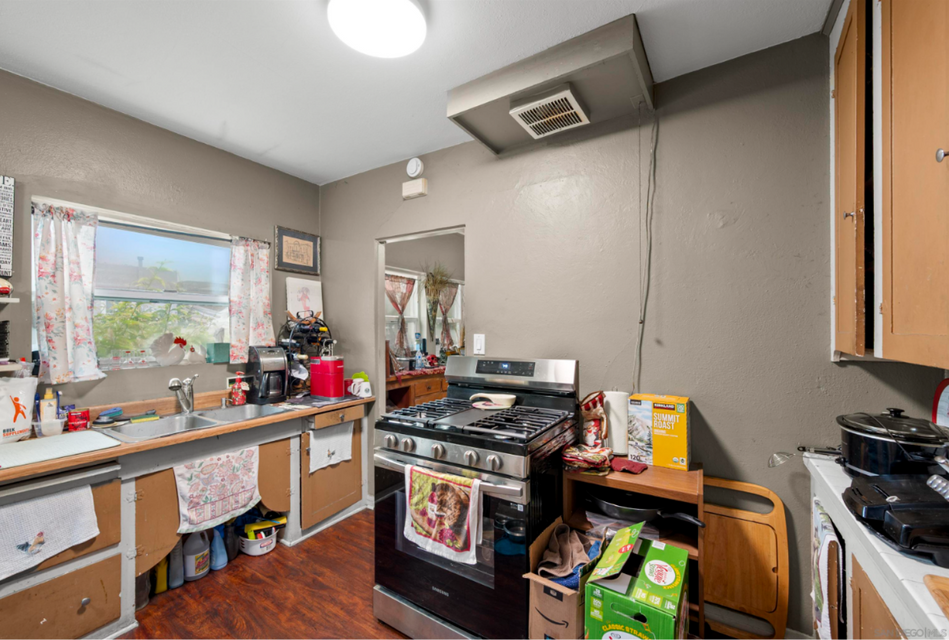 Small kitchen with stove, sink, countertop clutter, and a window on the left.