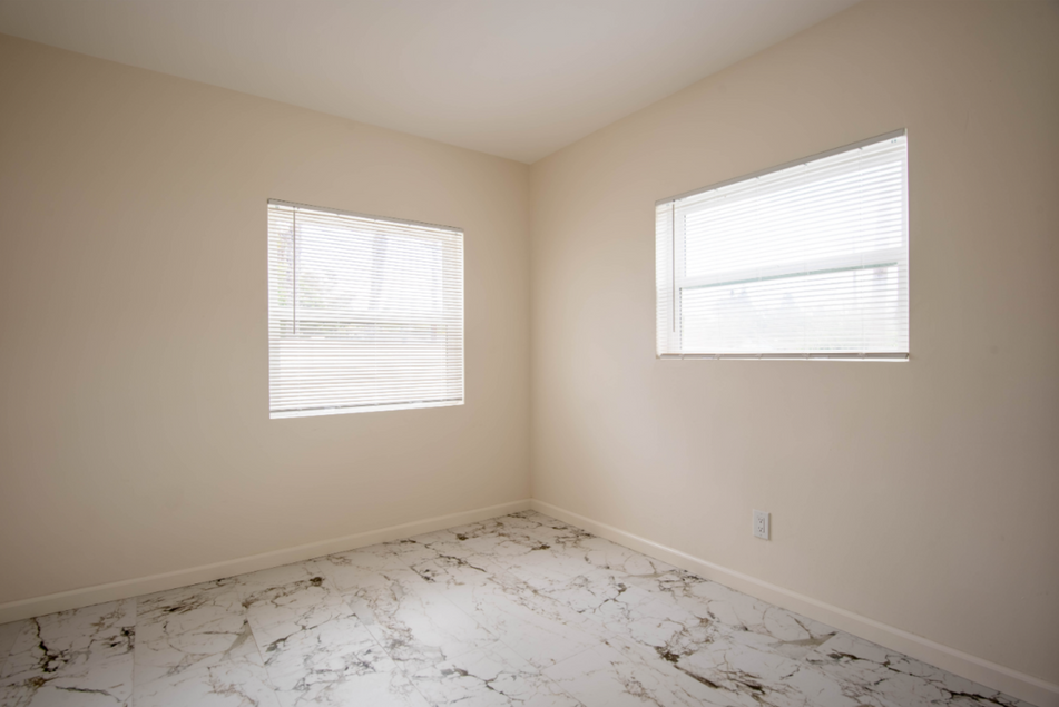Empty beige room with two windows and white marble-pattern tile floor