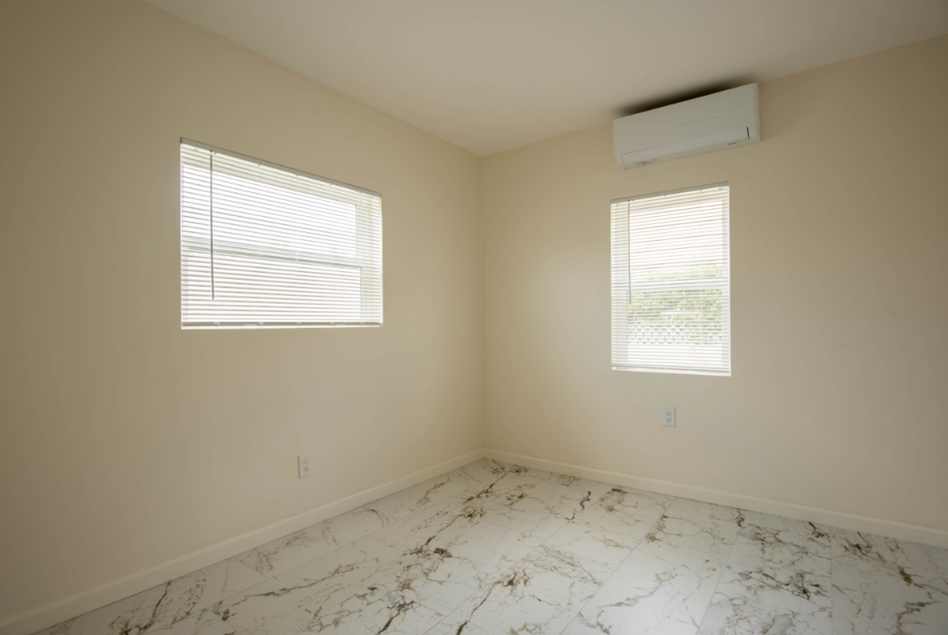 Empty beige room with marble-pattern tile floor and two windows with blinds