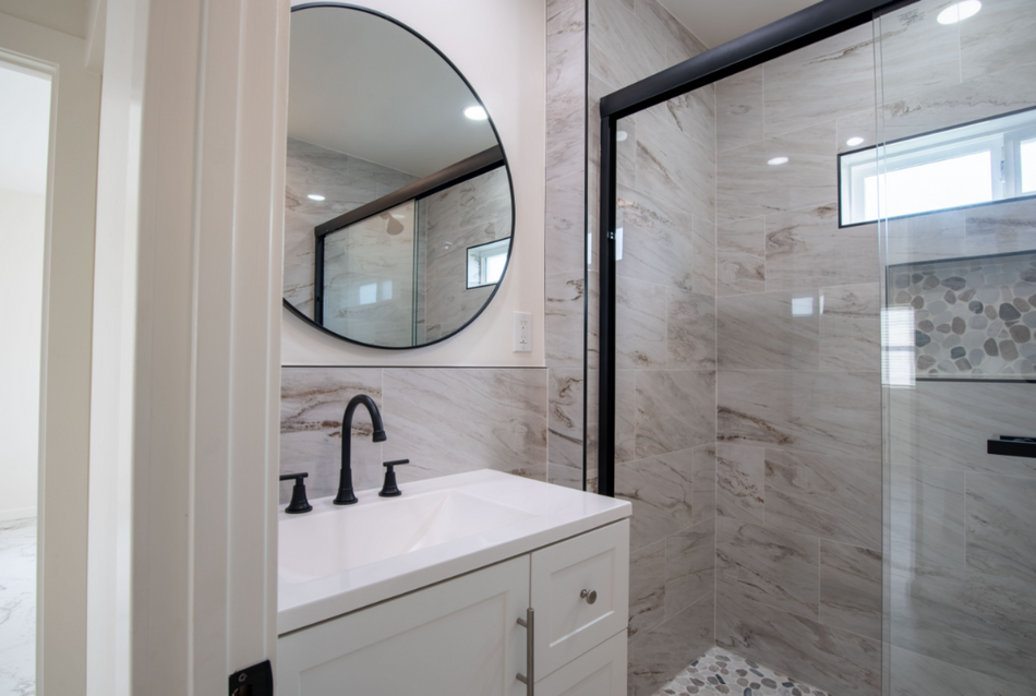 Modern bathroom vanity with round mirror, black faucet, and glass shower enclosure