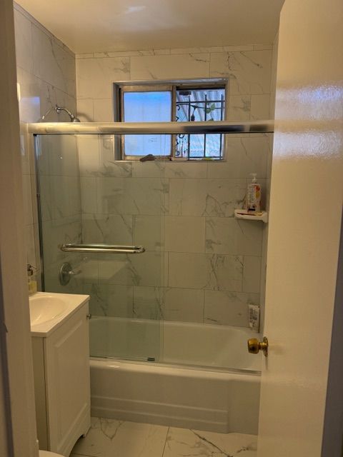 Bathroom with marble tile walls, a bathtub, and a glass shower door.