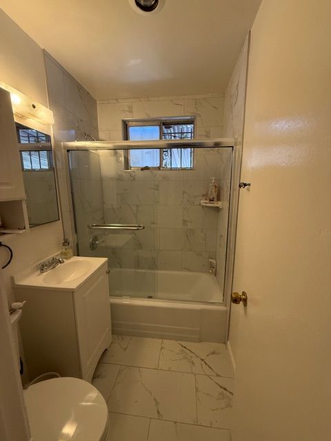 Small bathroom with white fixtures, marble-look tile, shower/tub combo, and window.