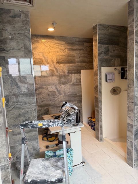 Bathroom renovation in progress; tile walls, step stool, shower stall, and tools are visible.