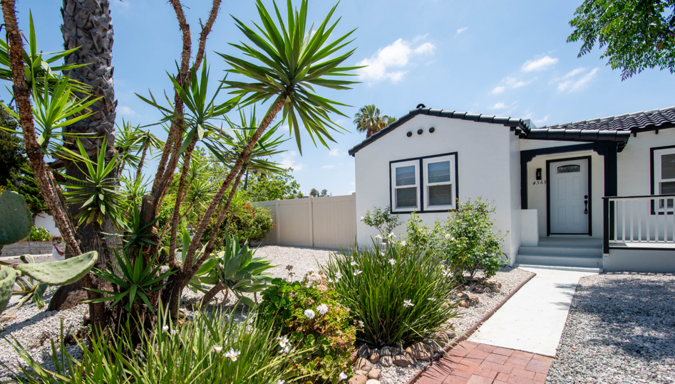 White stucco house with black trim, front porch, and desert landscaping under a sunny blue sky