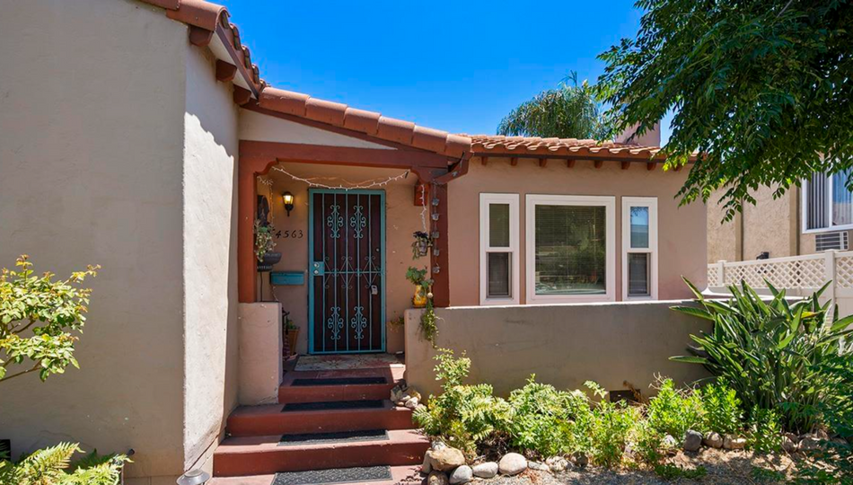 Stucco house entrance with red-tiled roof, iron security door, and front windows amid desert landscaping