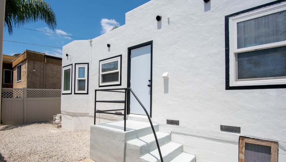 White stucco house exterior with black-trim windows, front steps, and a metal railing under a clear sky