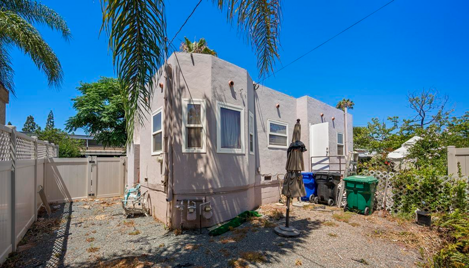 Small beige mobile home with a person outside, palm trees and a bright blue sky in a yard.