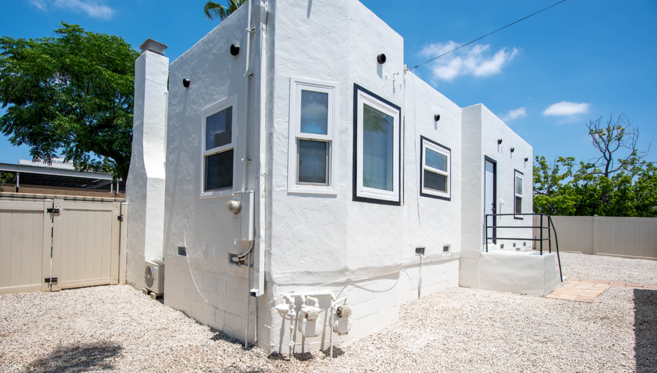 White modern house exterior with multiple windows, gravel yard, and a side gate under a blue sky
