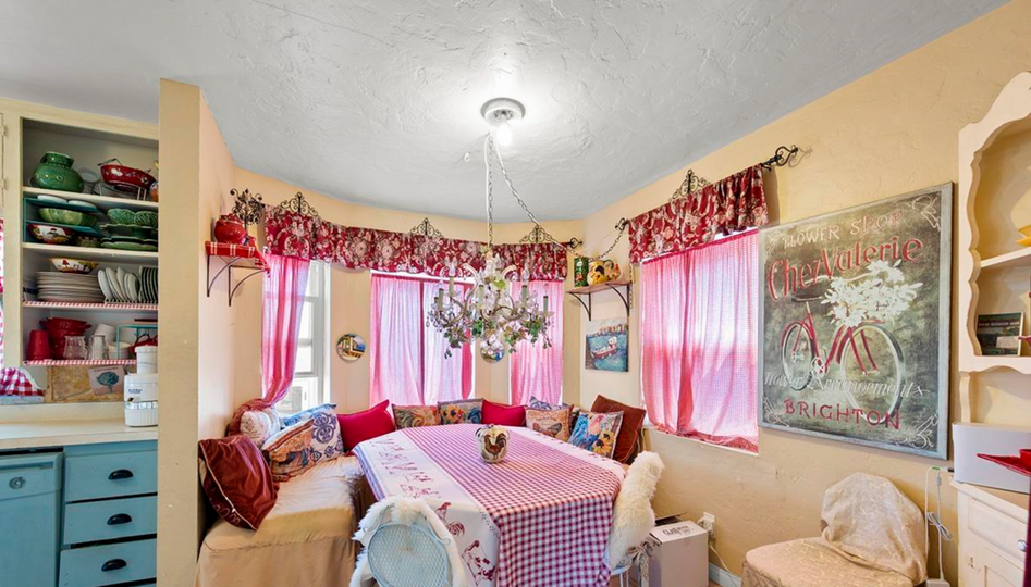 Bright dining nook with pink accents, round table, window seats, hanging plant, and wall art