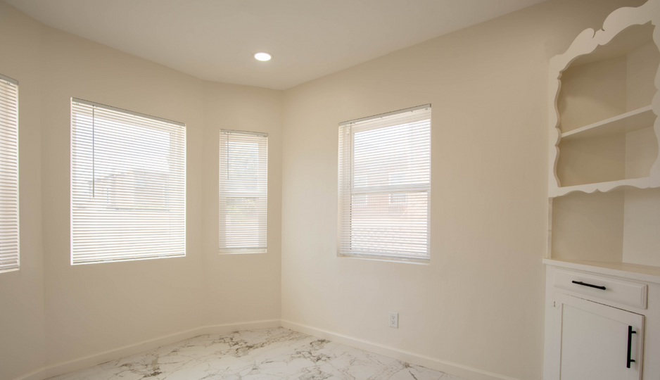 Empty beige room with three windows, marble floor, ceiling light, and built-in shelves