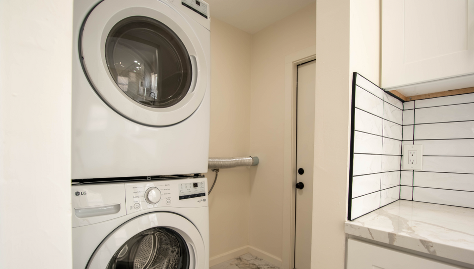 Stacked washer and dryer in a small laundry nook beside a tiled countertop and door.