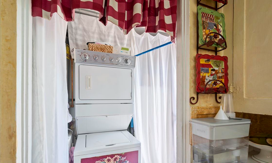 Cozy kitchen nook with a white stacked washer and dryer beside a red-and-white curtain and wall art.