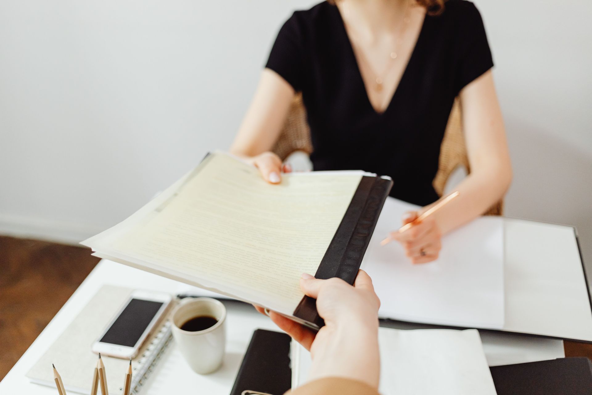 Two people reviewing an open notebook at a white table with a coffee cup and smartphone nearby