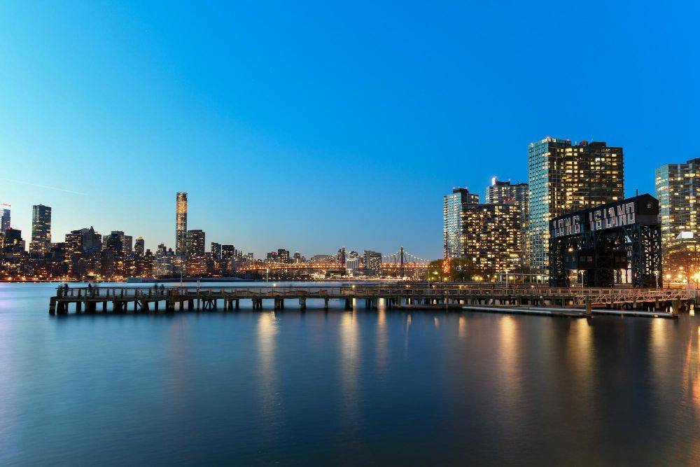 City skyline at dusk with illuminated buildings reflecting on calm water