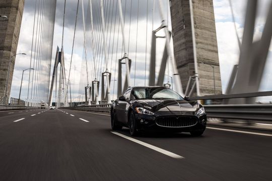 Black sedan driving on a cable-stayed bridge under cloudy skies