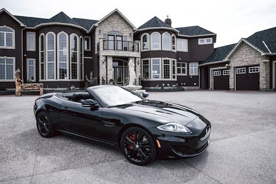 Black sports car parked in front of a large suburban house and garage