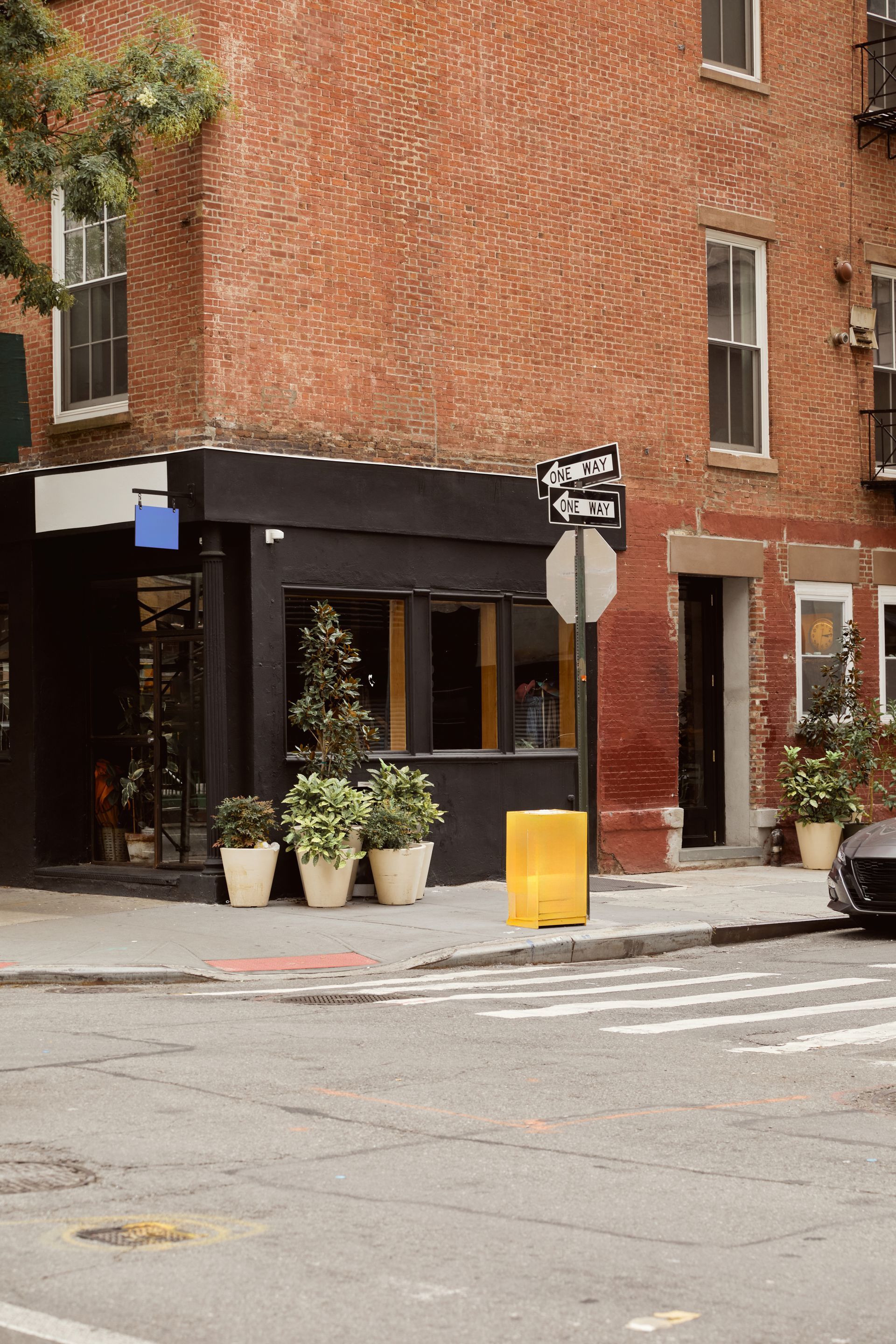 Street corner with a brick building, sidewalk café entrance, potted plants, and a stop sign