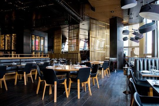 Modern restaurant dining room with wooden tables, black chairs, and warm industrial lighting