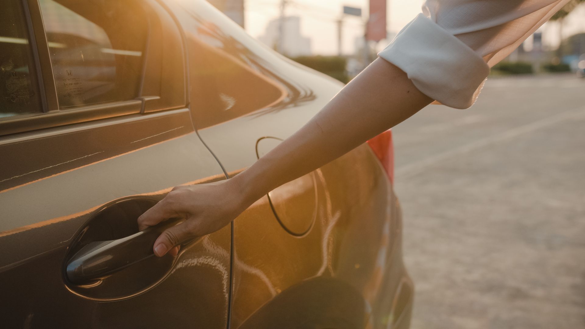 Hand reaching for the door handle of a parked car in warm sunlight