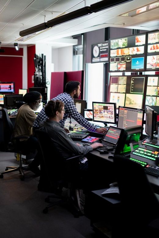 People working at a control room with multiple monitors and bright display screens
