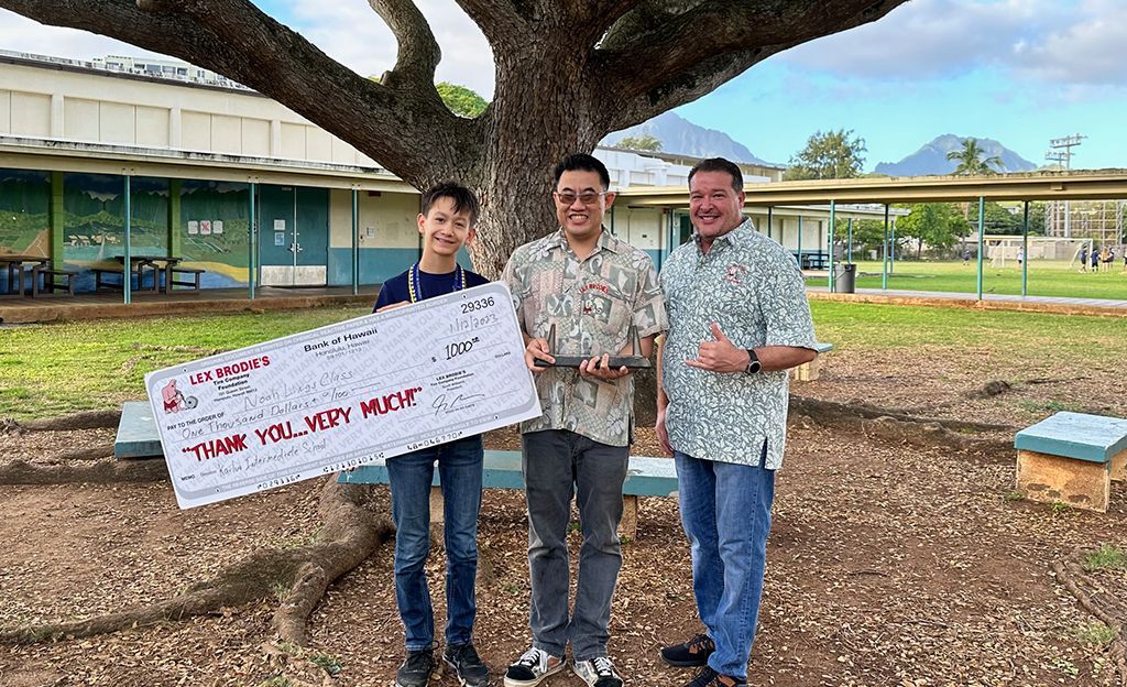 Three men are standing under a tree holding a large check. | Lex Brodies