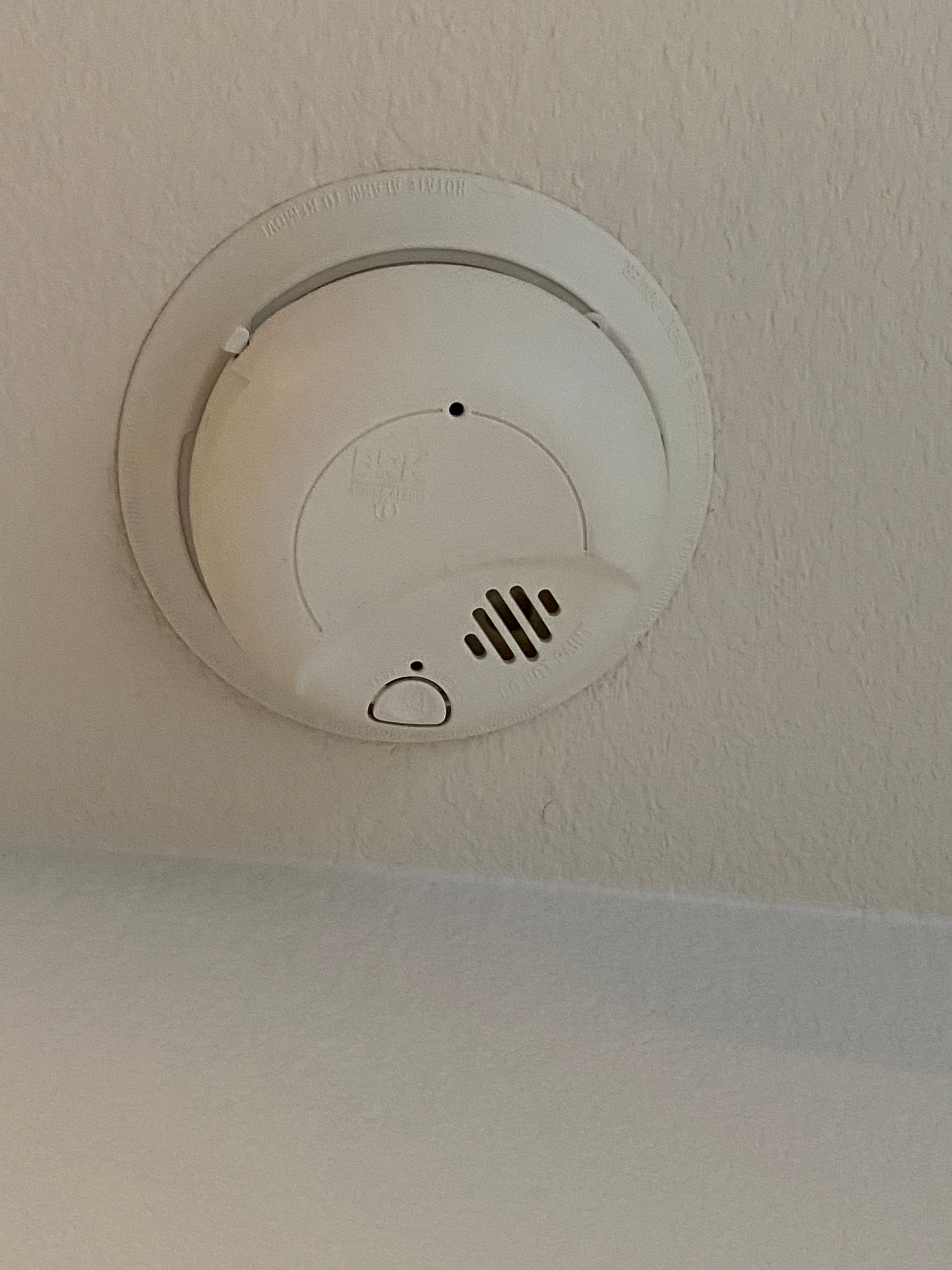 Ceiling-mounted smoke detector with a small vent grille on a white ceiling.