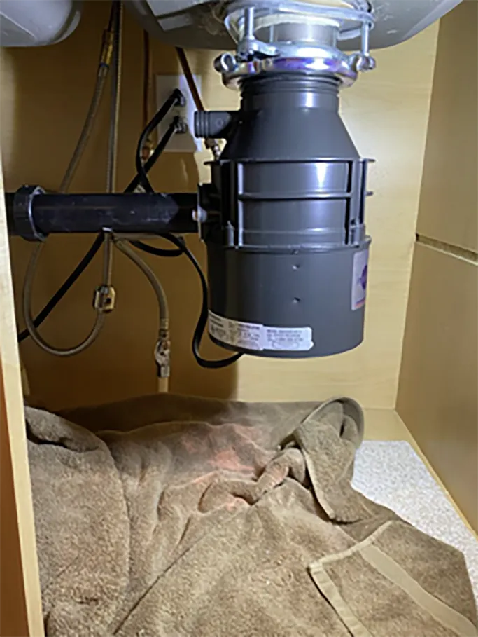 Garbage disposal under a kitchen sink with a towel or cloth beneath it