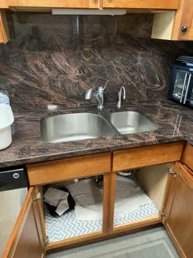 Kitchen sink under counter with open cabinet doors, exposed plumbing, and a microwave on the right.