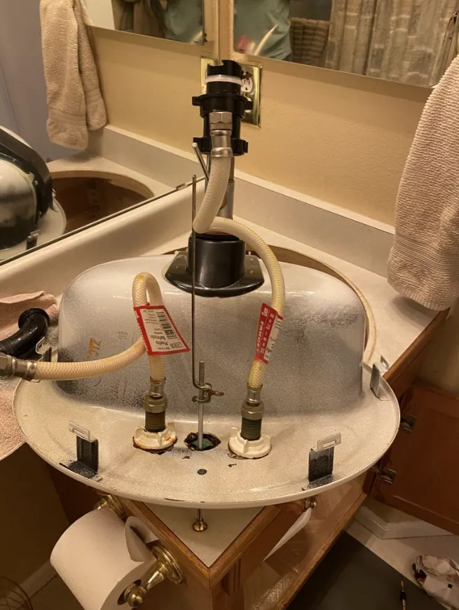 Bathroom sink with the vanity removed, exposing plumbing and hoses beneath the basin