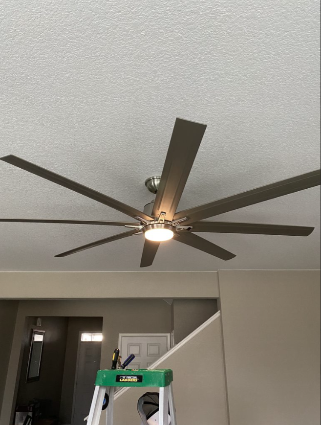 Modern ceiling fan with dark blades on a textured white ceiling, above a room interior.