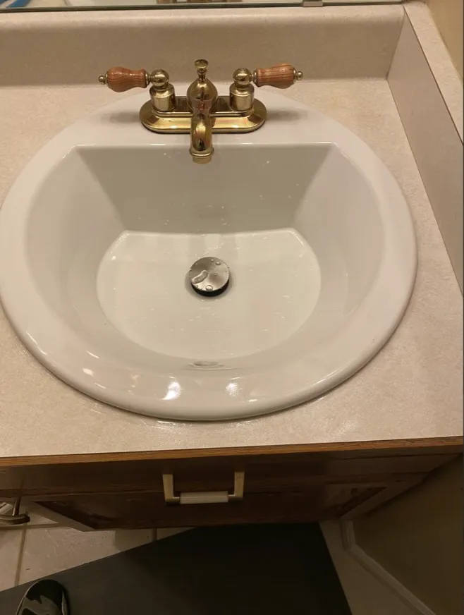 White bathroom sink with brass faucet and beige countertop, viewed from above