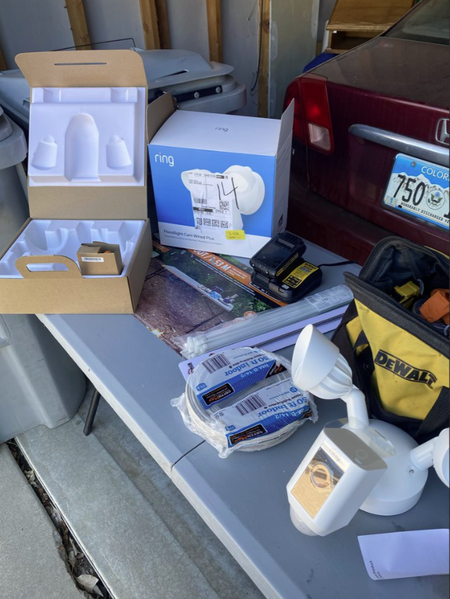 Open garage workbench with assorted tools, Ring doorbell boxes, and cleaning supplies next to a red car.
