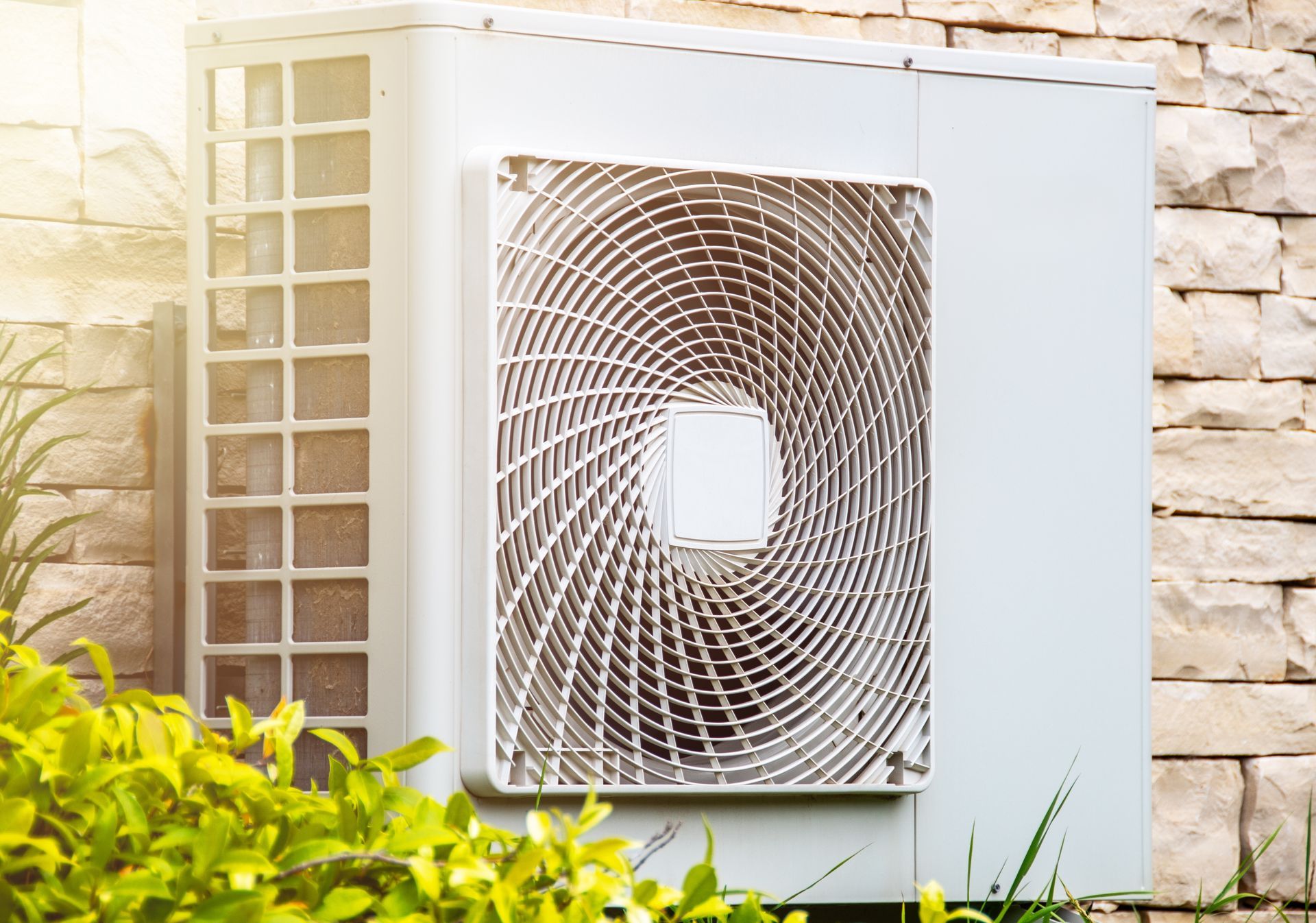 Wall-mounted outdoor air conditioner with a circular fan cover on a stone house wall.