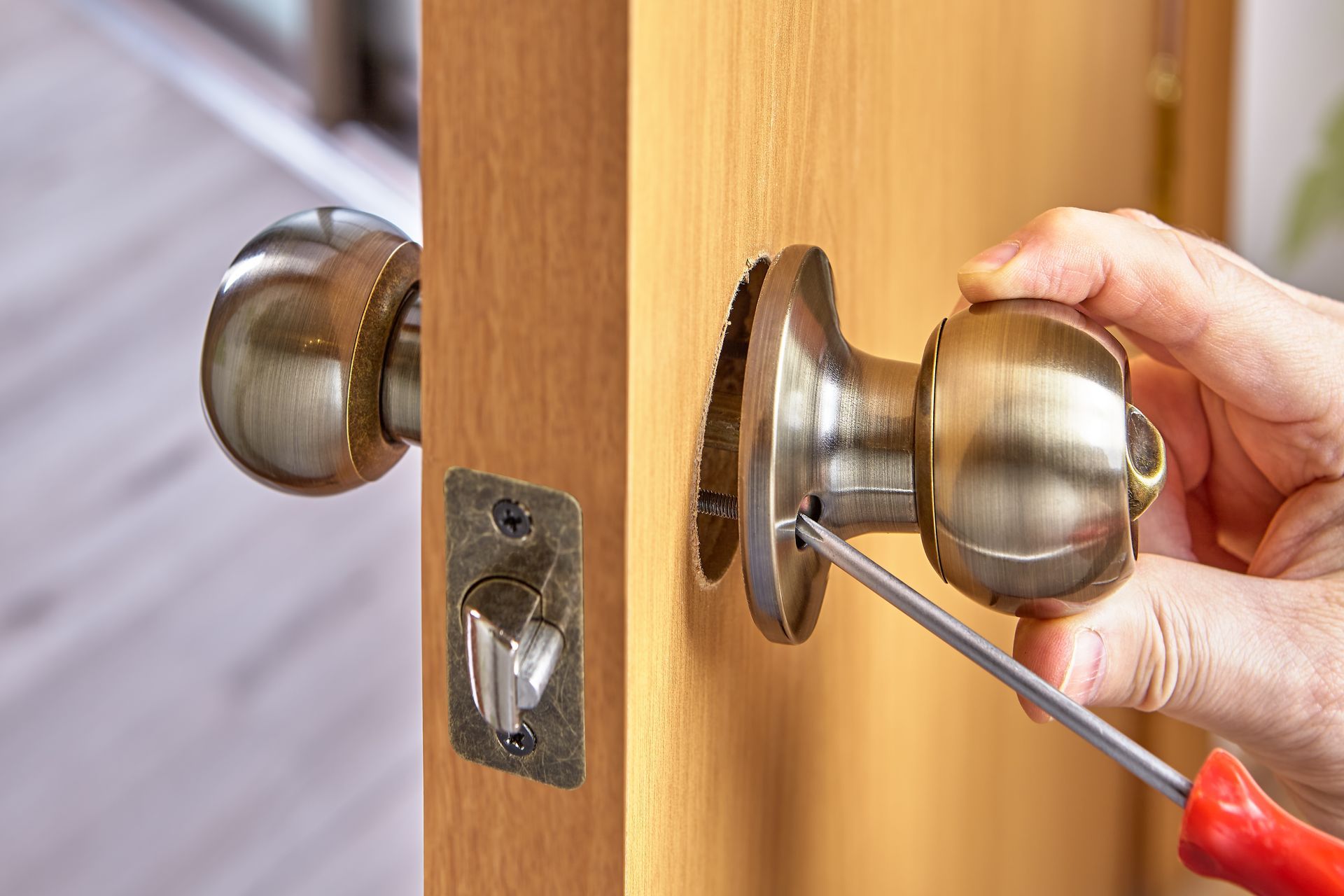 Hand using a screwdriver to install a brass door knob on a wooden door