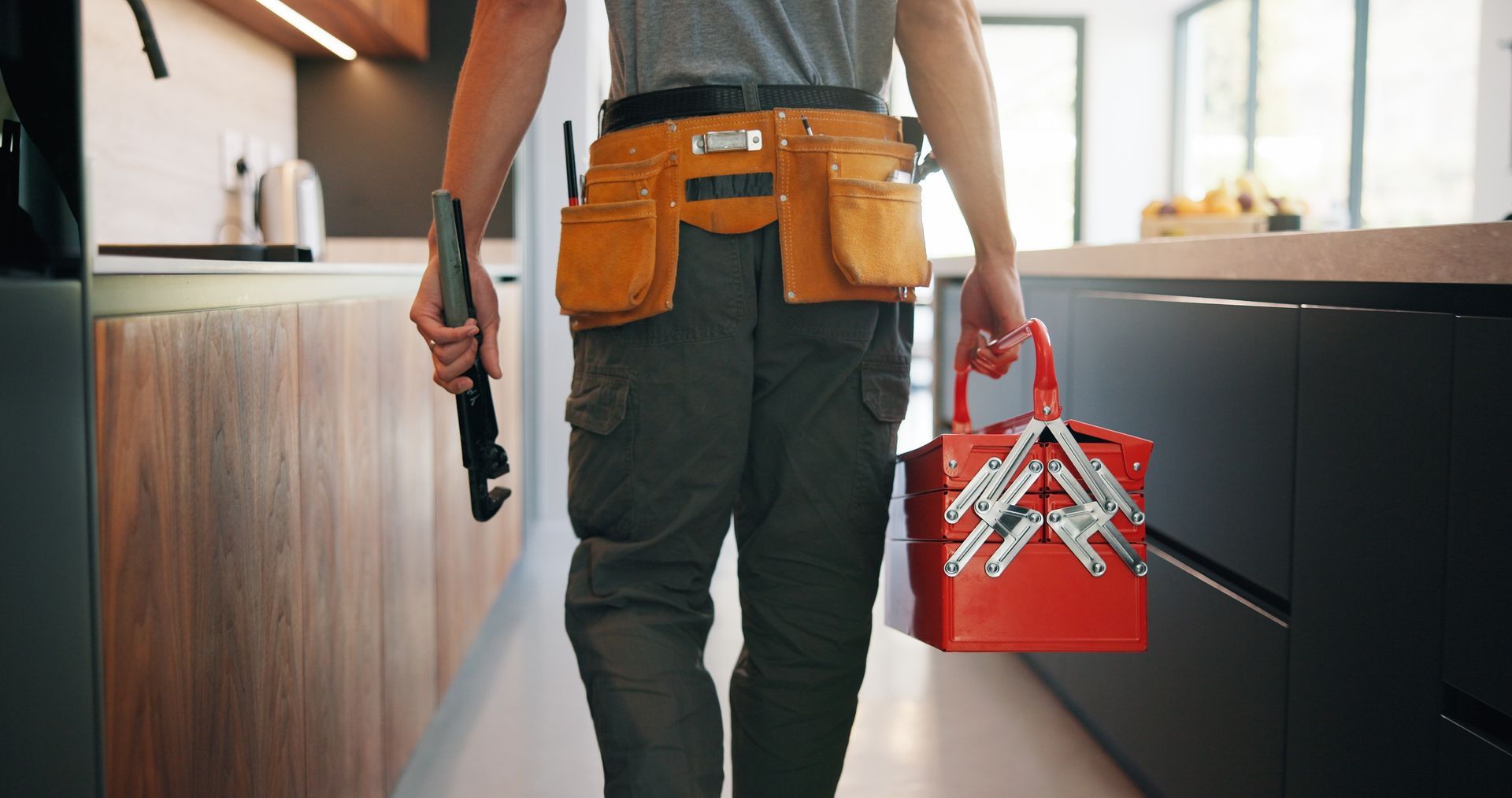 Person carrying a power drill and red toolbox in a home kitchen renovation scene
