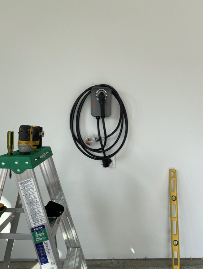 White wall with a coiled black cord, an aluminum ladder, and a yellow level leaning nearby
