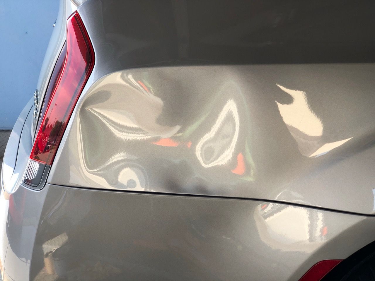 Dented silver car rear panel with a cracked taillight