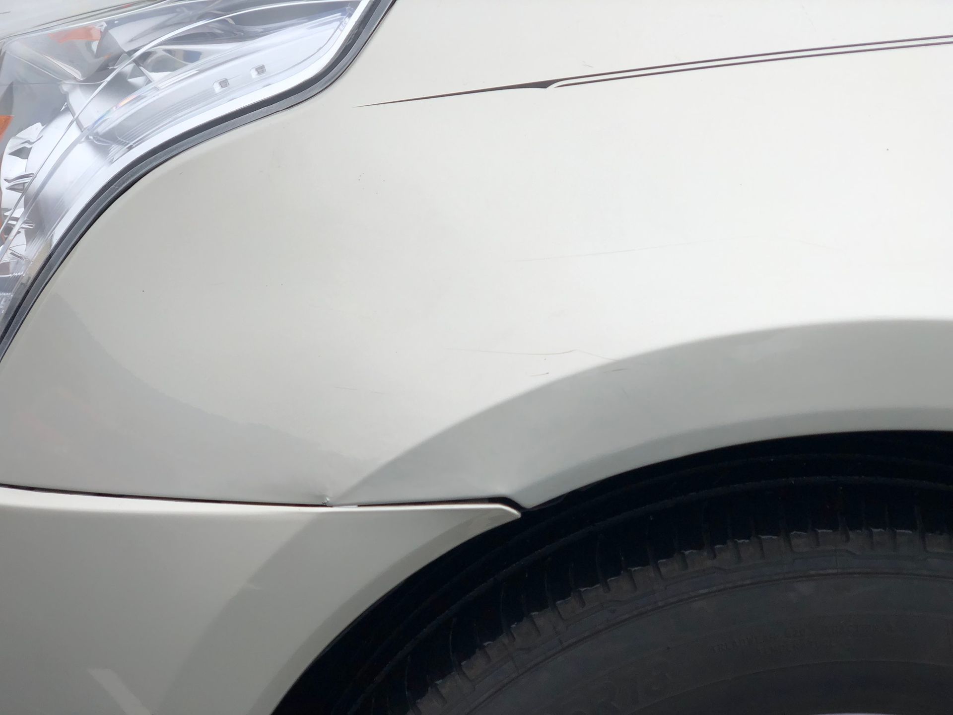 Close-up of a white car’s front fender and headlight above the wheel arch