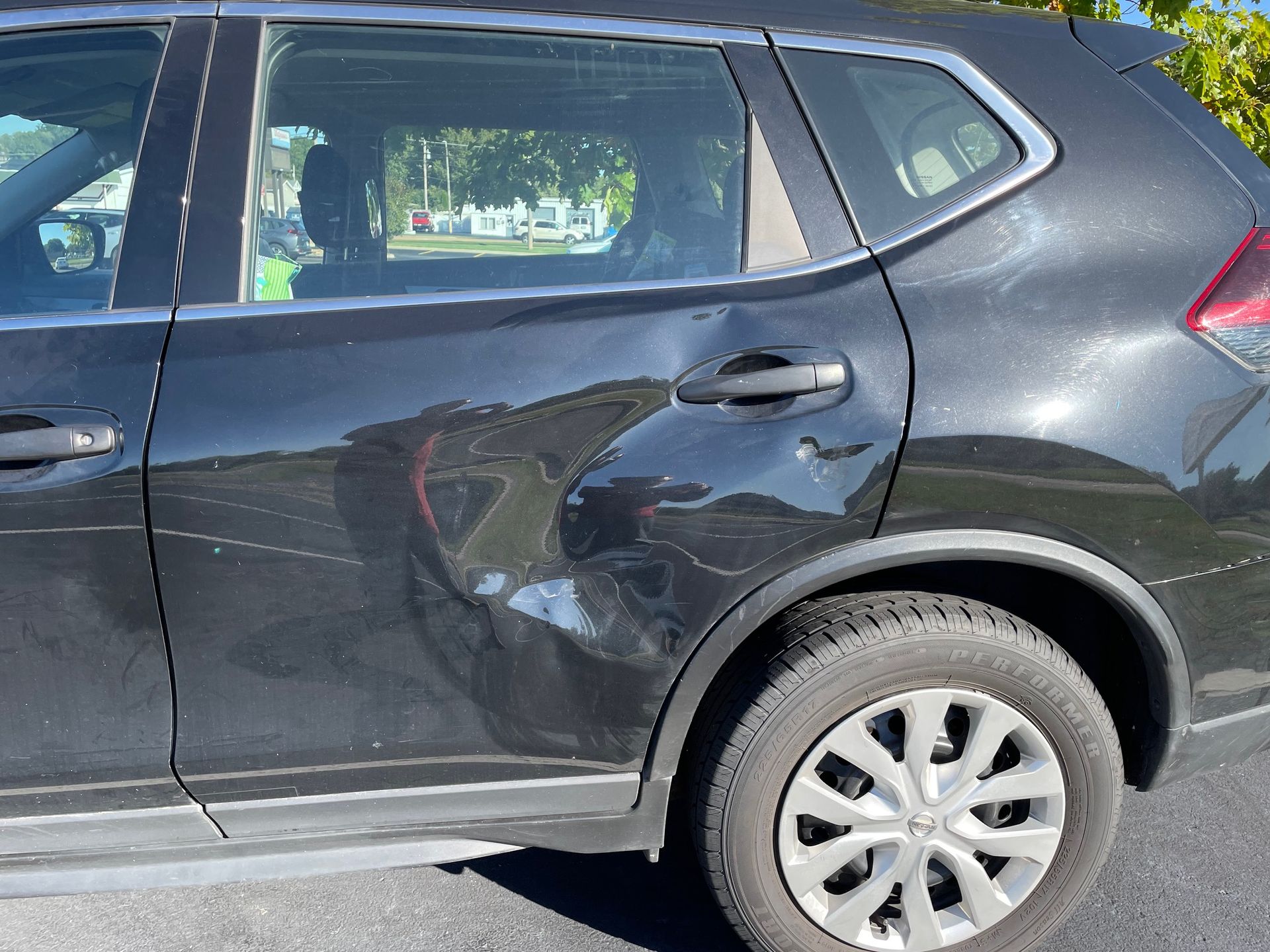 Dark gray SUV with a dent on the rear passenger door, parked outdoors.