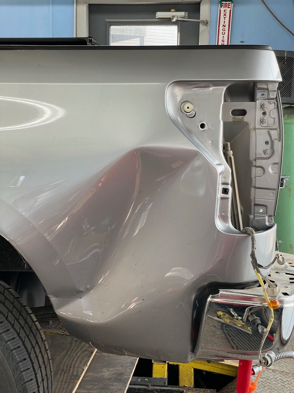 Damaged silver car rear quarter panel with crumpled metal and exposed taillight area
