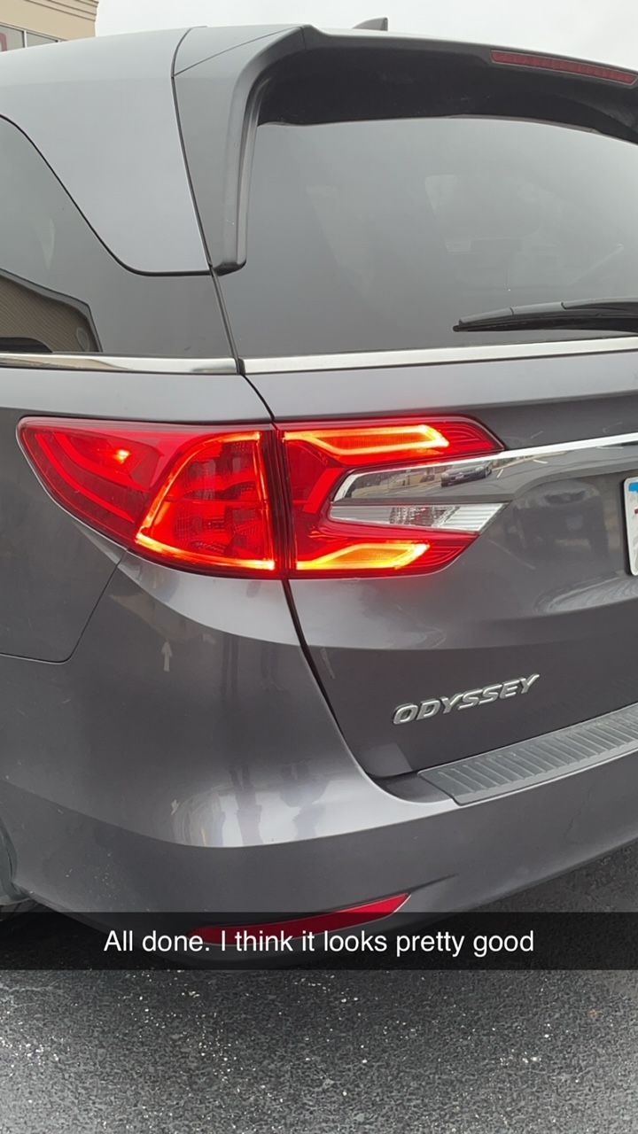 Close-up of a gray Honda Odyssey rear, with the left taillight illuminated in a driveway.