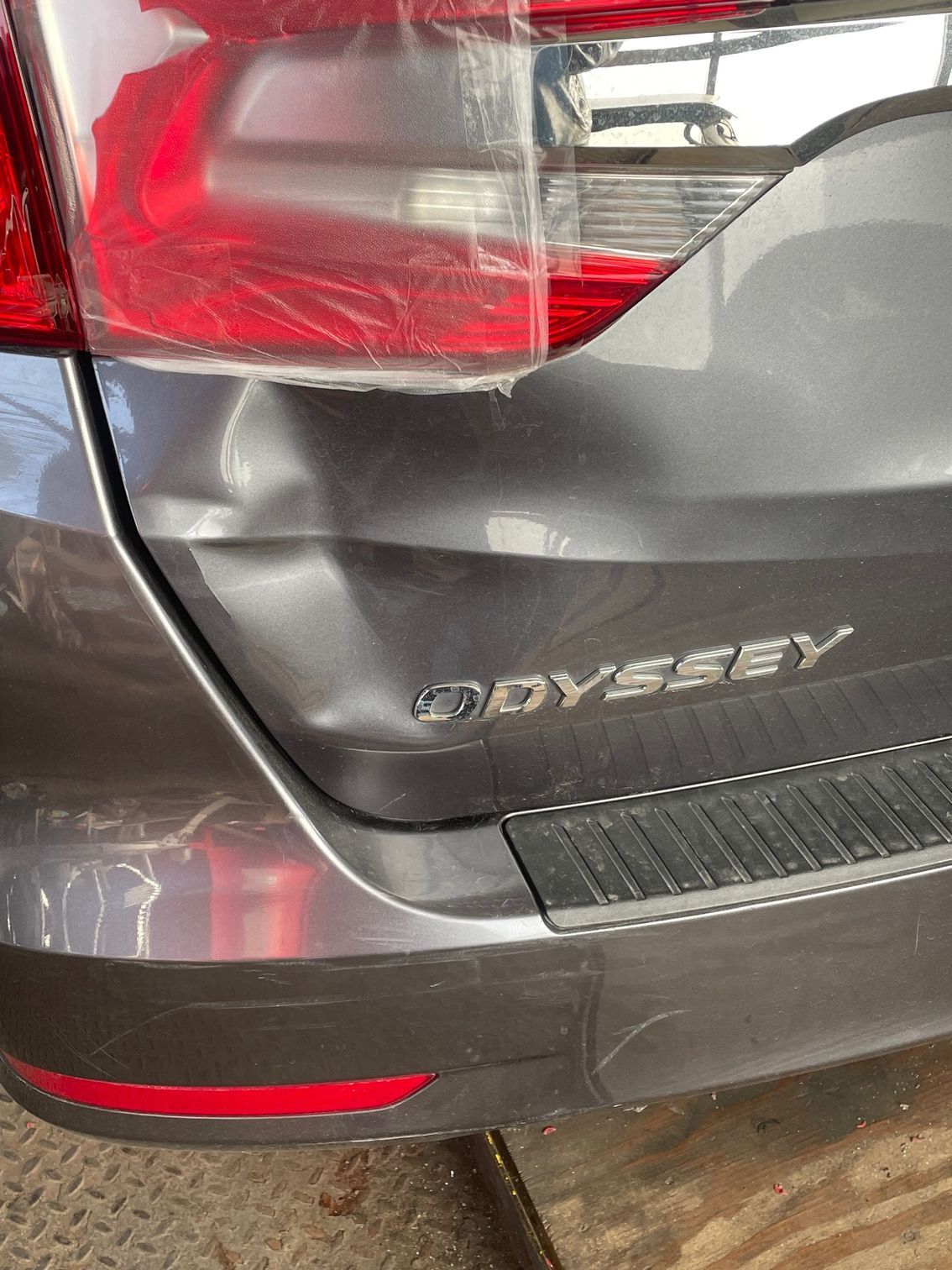 Rear view of a gray Toyota Odyssey with a dented tailgate and left taillight visible
