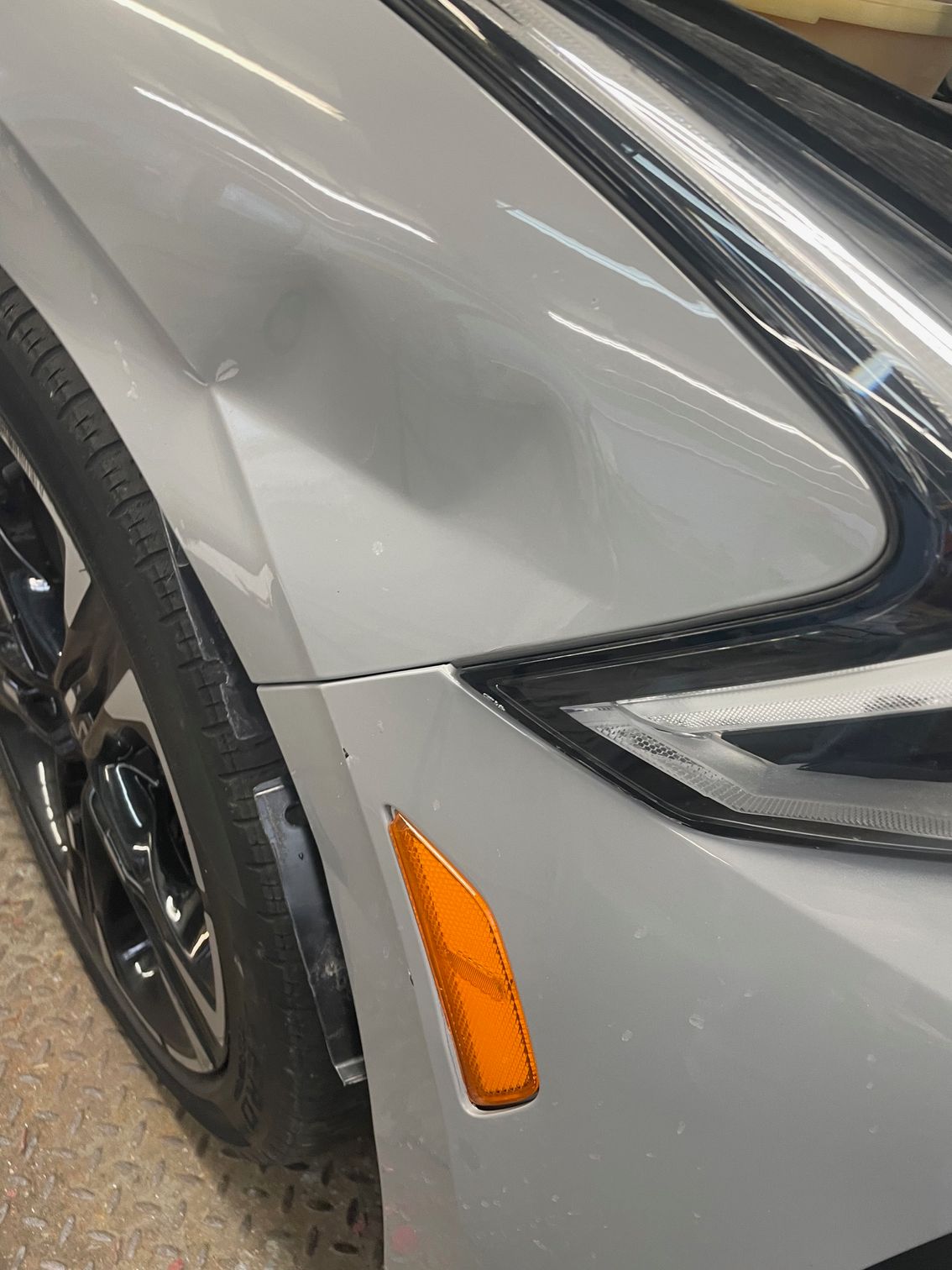 Close-up of a silver car’s front fender, wheel, and amber side marker light