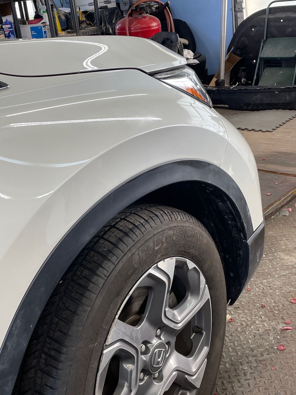 Silver SUV front wheel and fender in an auto repair shop with tools and equipment in the background