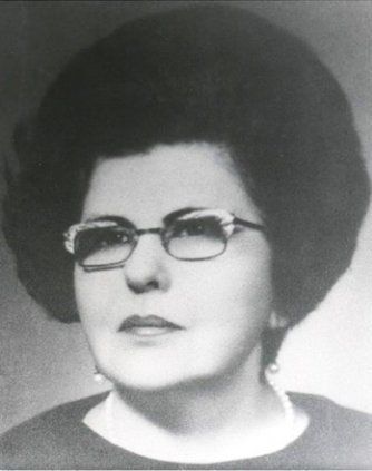Woman with large dark hair, glasses, and a serious expression.