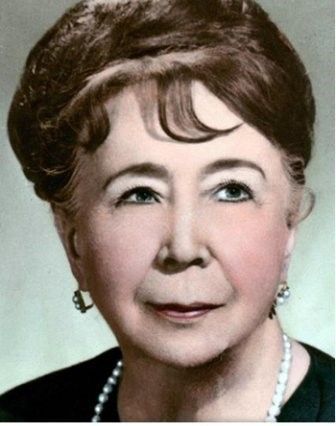 Woman with dark hair, wearing a pearl necklace and earrings, smiling slightly.